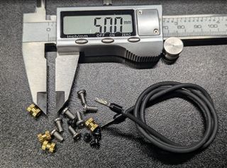Fasteners laid out beside a digital caliper for scale: brass heat-set inserts, M3 screws, small black self-tapping screws for the display, and the black bonding wire with a terminal on one end