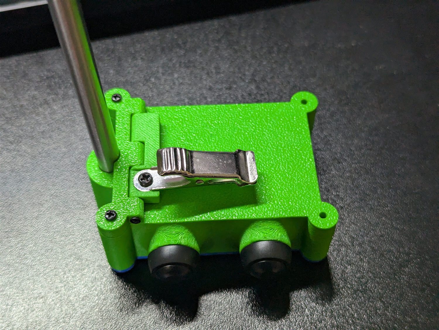 Close-up of the stainless spring clip screwed between the two printed holders on the green body, with the probe passing through alongside