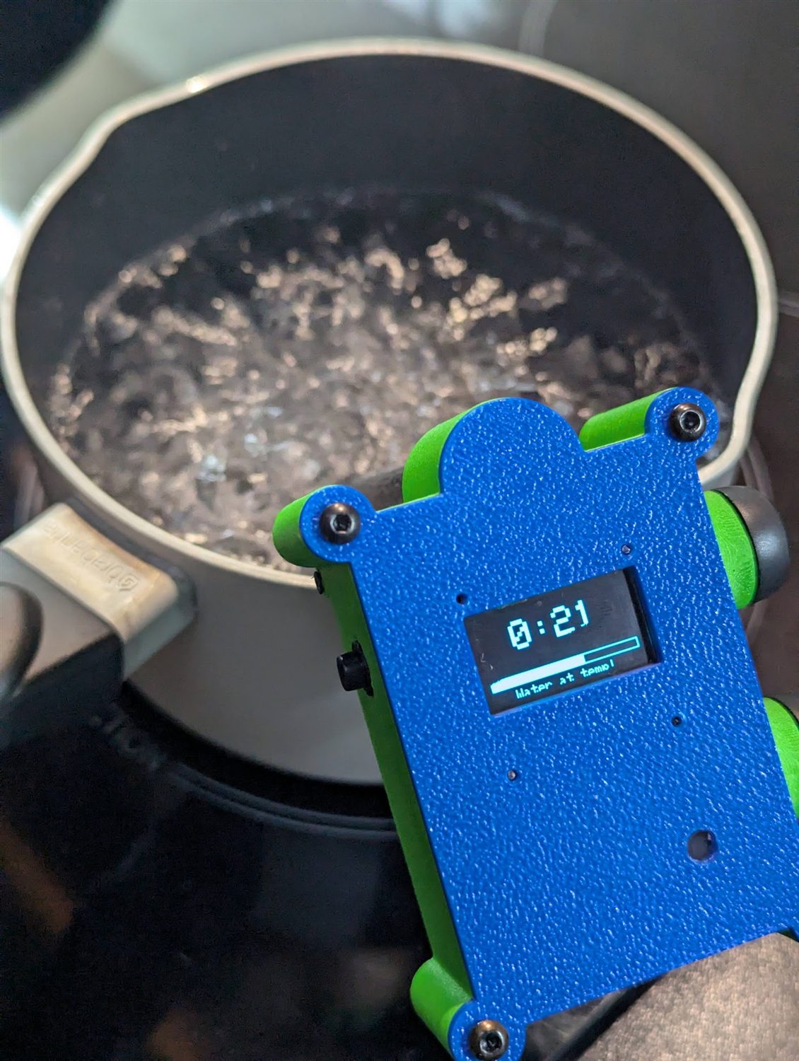 The same device counting down from twenty-one seconds, captioned Water at temp, over a pot at a full rolling boil